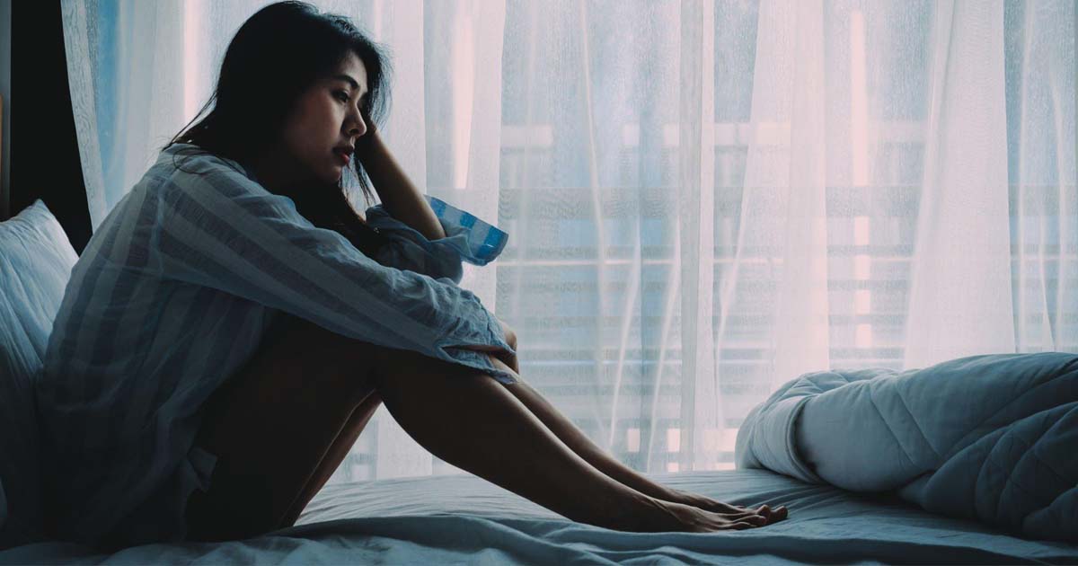 Asian woman sitting on a bed looking sad