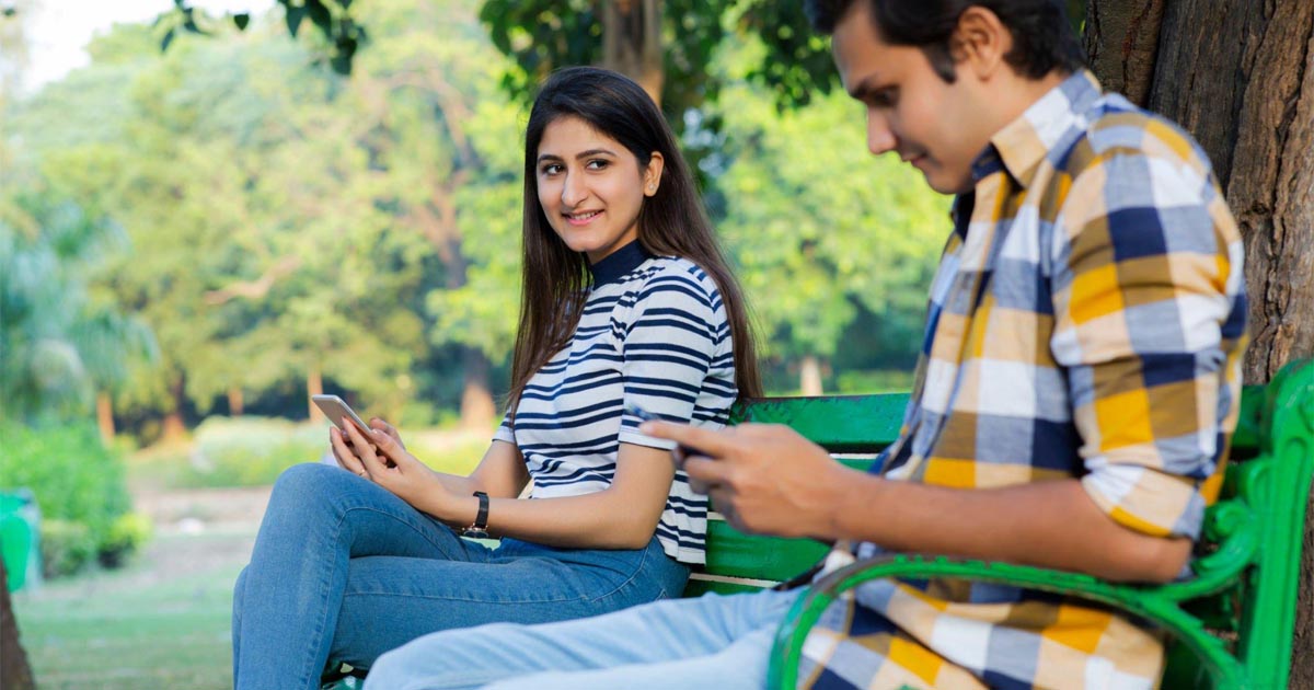 Young couple in the park texting on smartphones